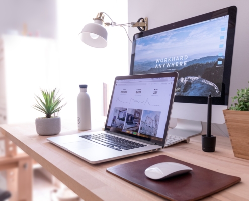 A laptop sitting on a desk with a large monitor, plant, and water bottle. Featured in Digital Agent's Internet Guide for Small Businesses